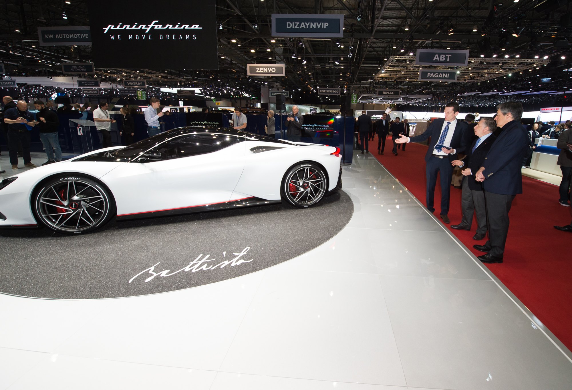 A white Pininfarina Battista hypercar on its motor show stand with visitors gathered alongside