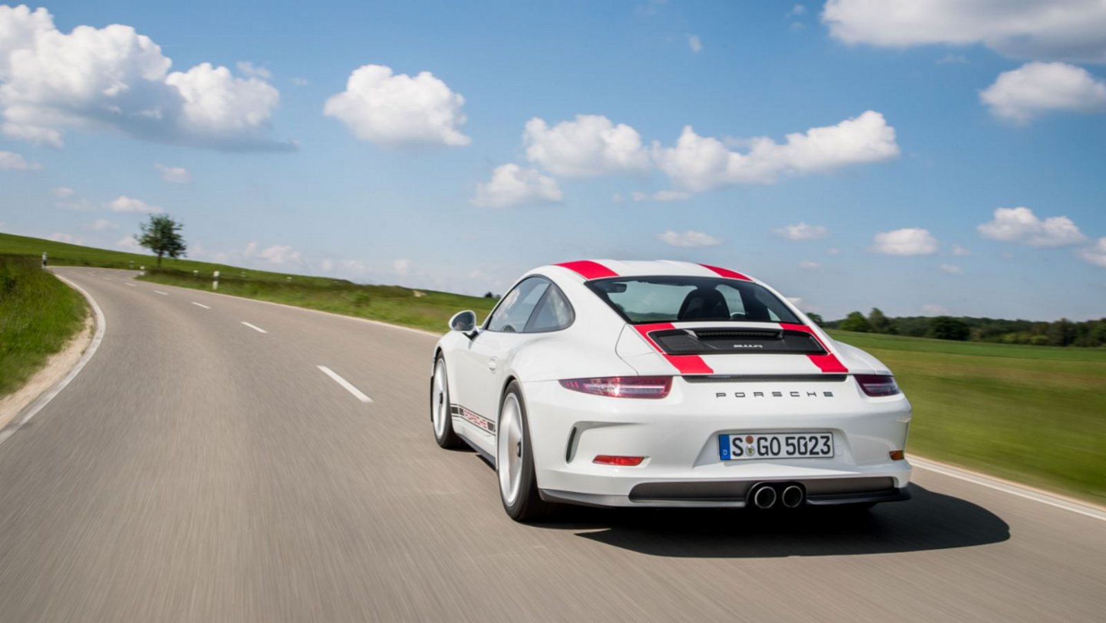 A white Porsche 911 with red stripes driving away on a country road under a blue sky